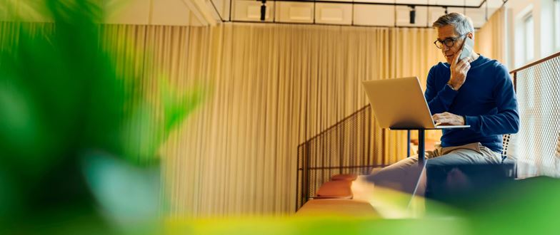 Professional using a laptop and phone in a modern office, supporting global workforce and compliance needs.