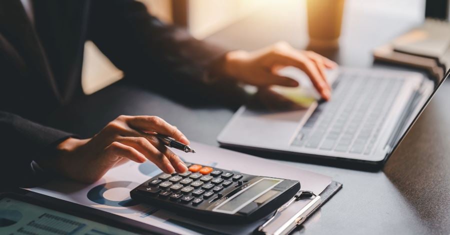 A woman sitting at a desk working on a laptop and a calculator