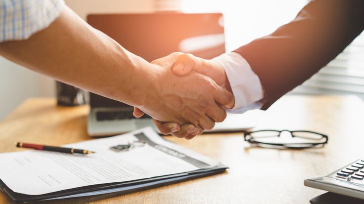 Two people shaking hands over a signed agreement
