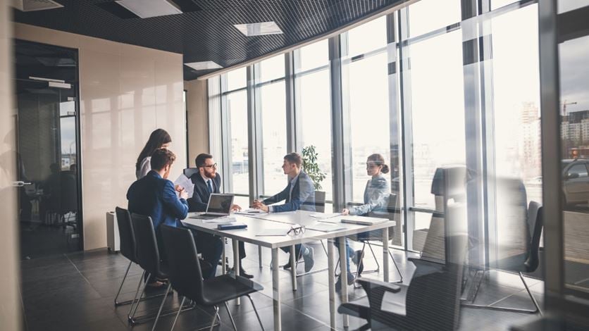 A group of men and woman in formal business wear sitting around a meeting table