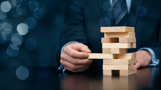 A suited man pulls a block out of a Jenga tower