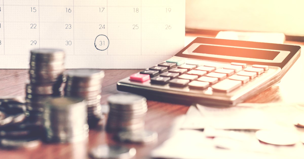 Coins in piles on a desk with a calculator and calendar in the background