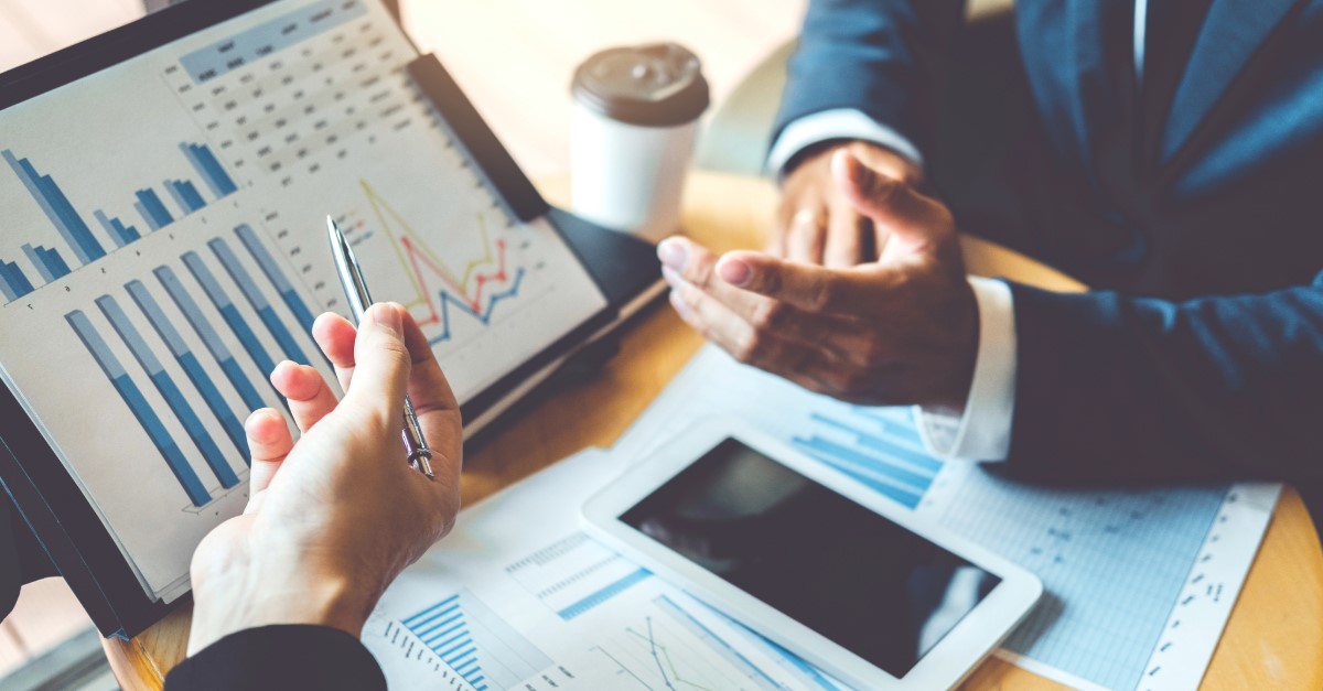 Two suited people discussing figures over various charts