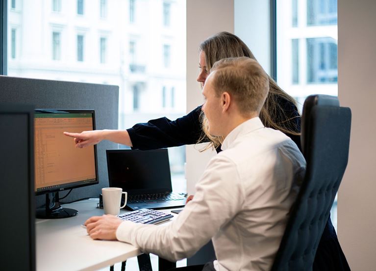  Kollegaer diskuterer forran pc-skjerm på kontoret.