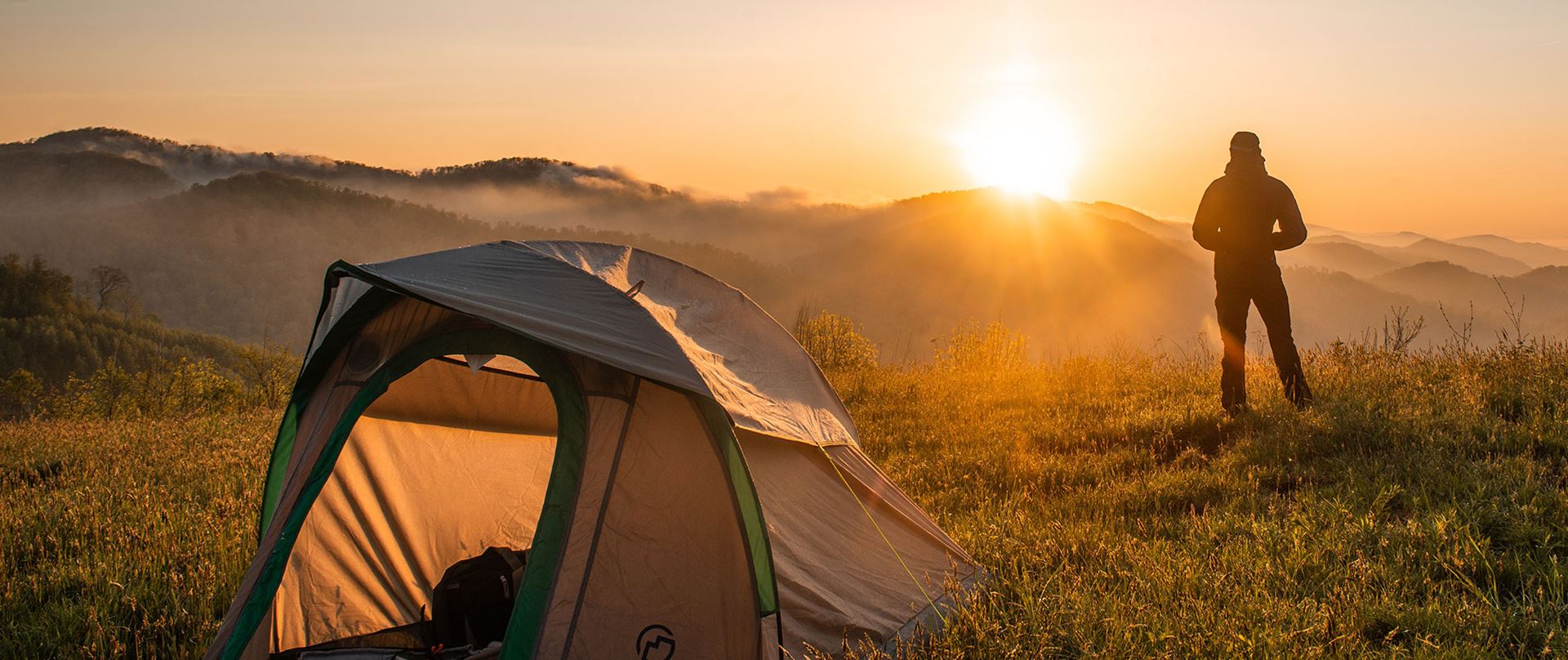 Person med telt som skuer over natur, fjell og soloppgang.