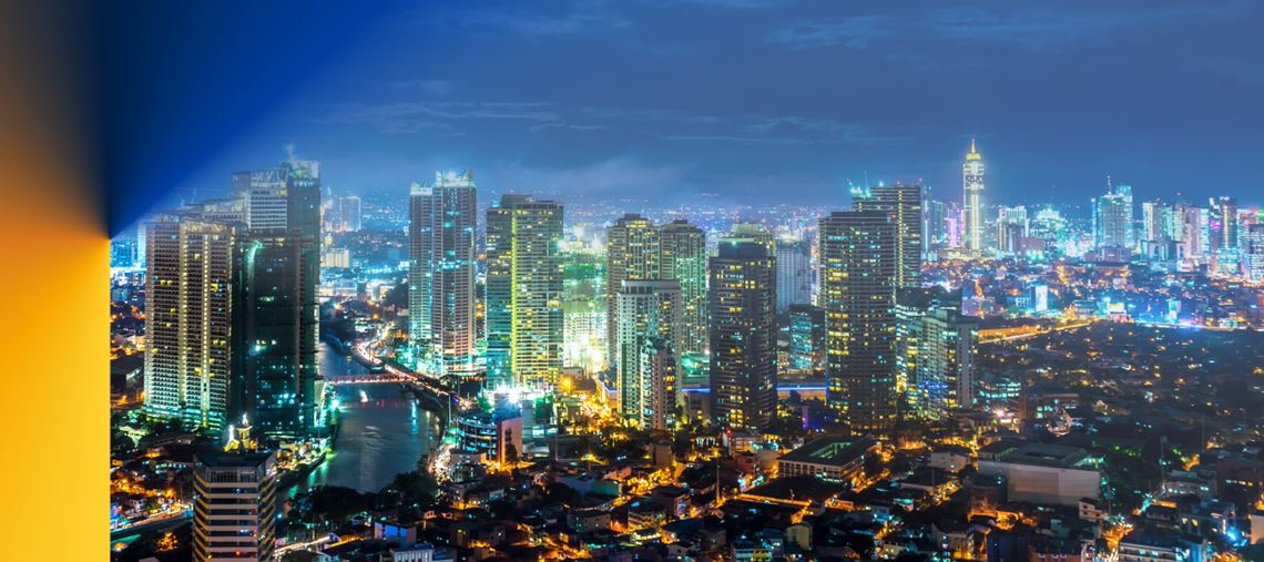 Photograph of the Makati skyline at dusk, showcasing the bustling business district where Crowe Philippines is located. The image captures a panoramic view of towering skyscrapers with their lights beginning to twinkle against the evening sky. Prominently featured buildings, reflective glass facades, and the dense urban layout symbolize the dynamic business environment of Makati. The setting sun casts a warm glow over the city, highlighting the mix of modern architecture and the vibrant atmosphere of this financial hub.