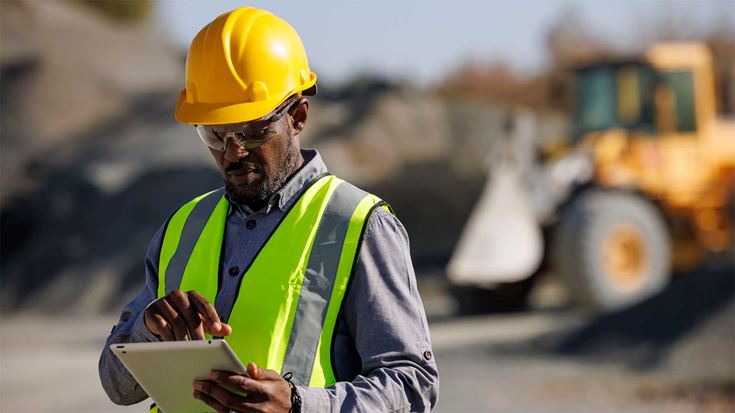 An engineer in a security vest and hat inspecting a site