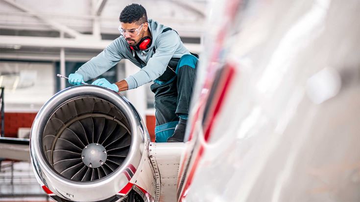 Engineer performing maintenance on a plane engine in an aircraft hangar.