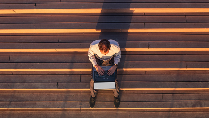 man on laptop sitting on steps in the sunshine