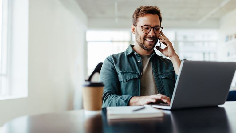 Man on phone and typing on laptop