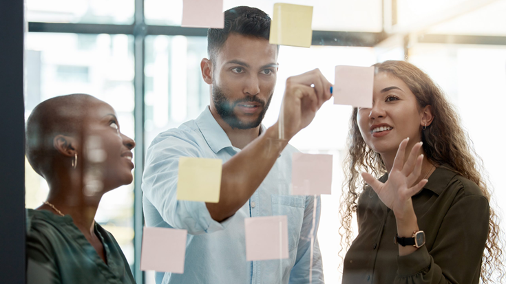 three people in a meeting looking at post it notes on a glass wall