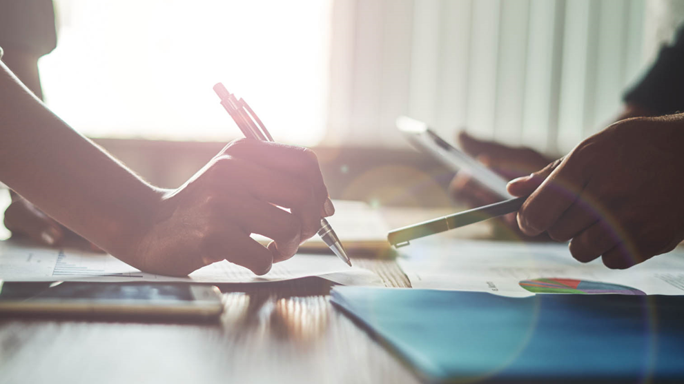 two people pens graphs on desk