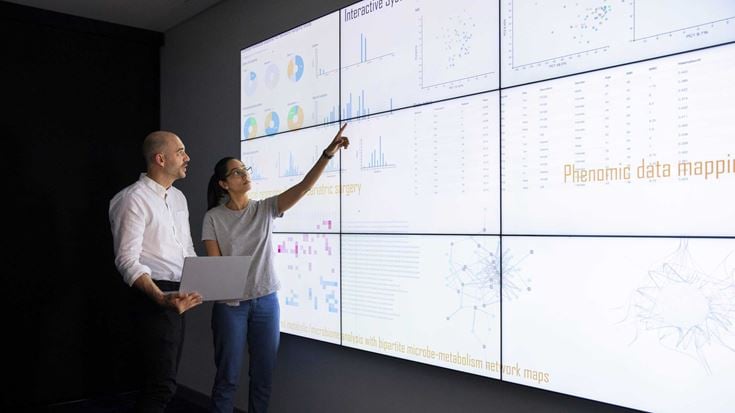 Two professionals looking at data on a big screen