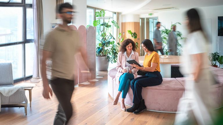 two women looking at tablet with people blurred