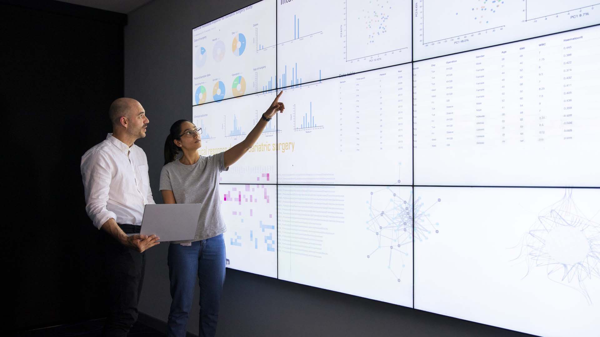 Woman and man looking at large screen with data