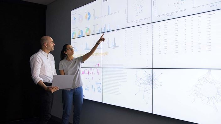 Woman and man looking at large screen with data
