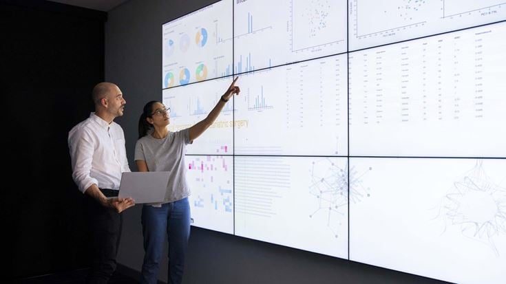 Woman and man looking at large screen with data