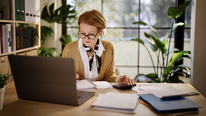 A female finance professional reviewing paperwork and using a calculator