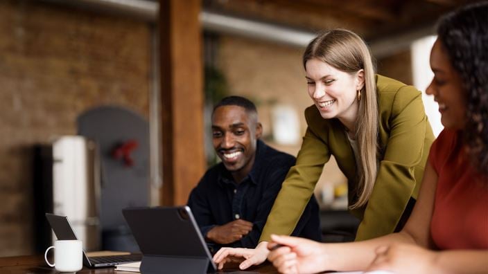 woman in green helping two people on laptop