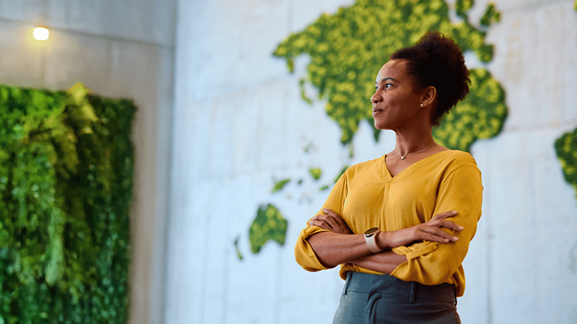 woman in yellow with arms crossed against a green map wall