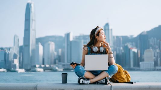 Woman sitting at riverside on laptop