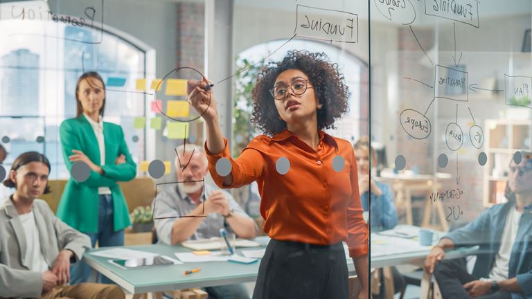 woman writing on glass board in meeting