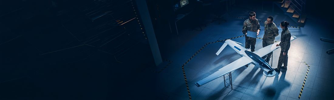 Defence and aerospace professionals reviewing an unmanned aircraft model in a UK defence supply chain engineering facility.