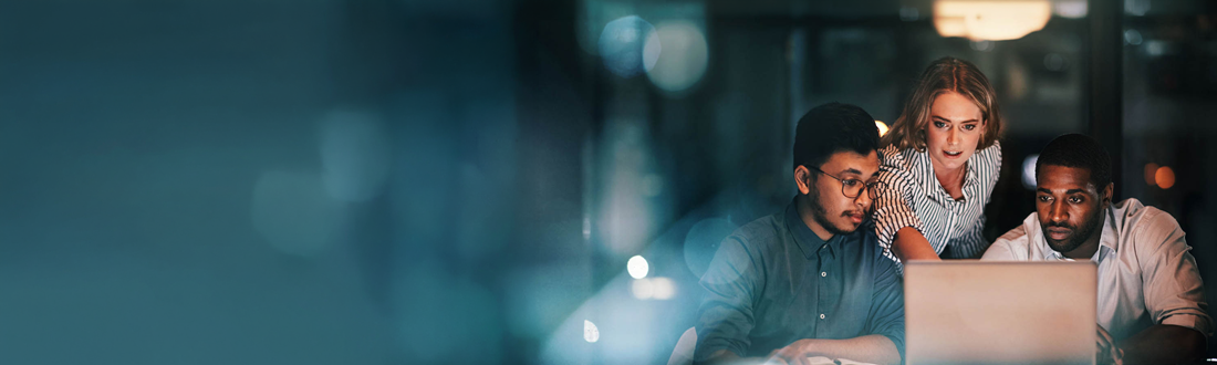 group of three people looking at a computer at night time