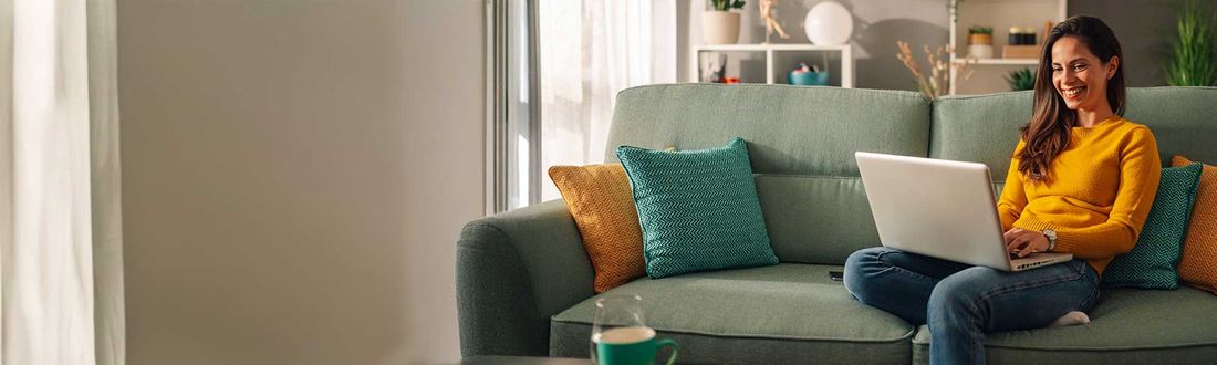 A woman in a yellow jumper working on laptop on the sofa at home