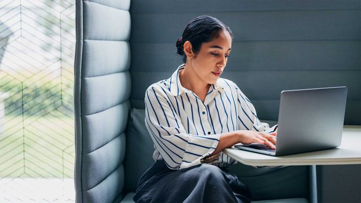 A professional woman working on a laptop in a booth