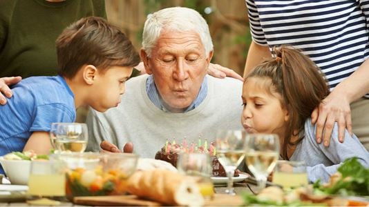 A grandfather blowing out birthday candles with grandkids