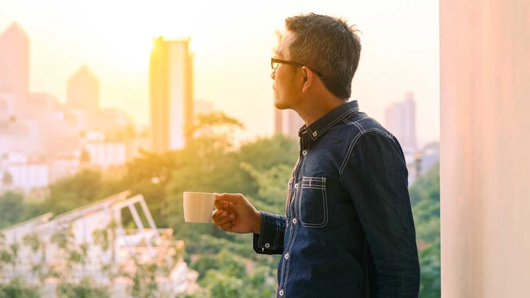 A man looking over city landscape holding a coffee cup