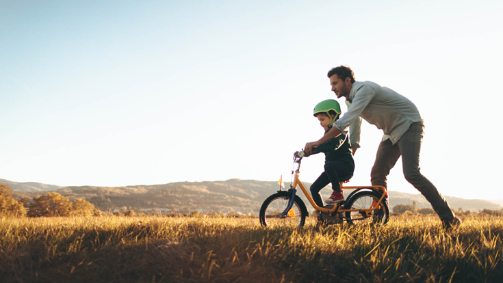 man teaching child how to ride a bike in a field