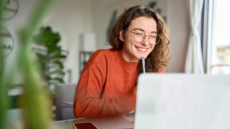 A young woman smiling whilst looking at laptop