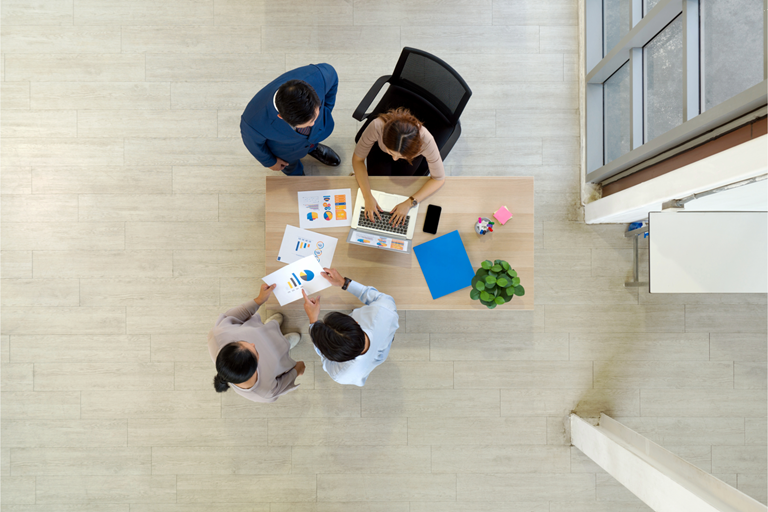Four business people meeting around a small table with document papers folder mobile phone and lapto