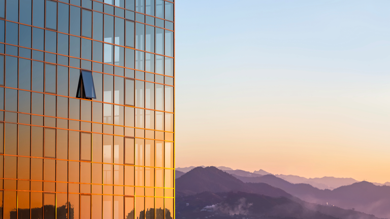 The glass wall of a modern building against the background of the sky and mountains